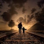 Father and son silhouettes walk on gravel railroad tracks at dusk, evoking child custody modification Wesley Chapel NC.