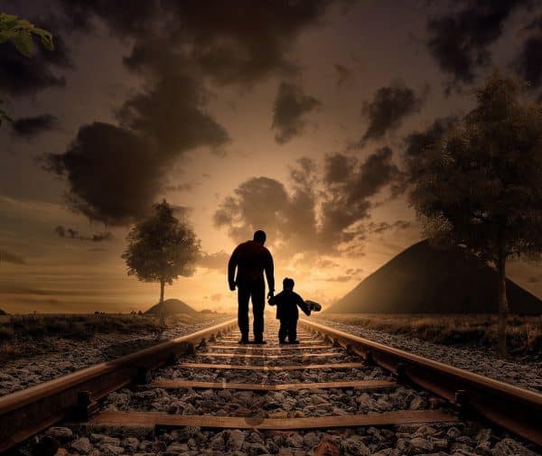 Father and son silhouettes walk on gravel railroad tracks at dusk, evoking child custody modification Wesley Chapel NC.