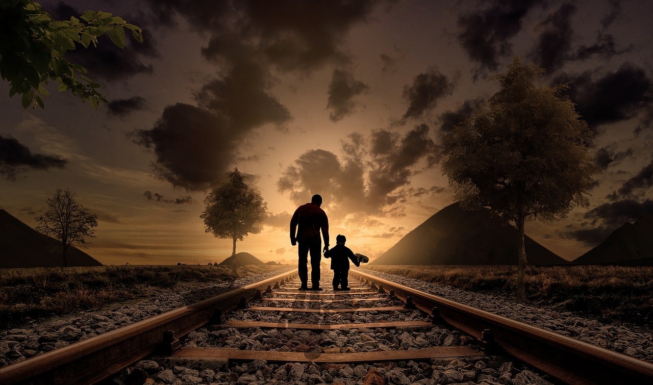 Father and son silhouettes walk on gravel railroad tracks at dusk, evoking child custody modification Wesley Chapel NC.
